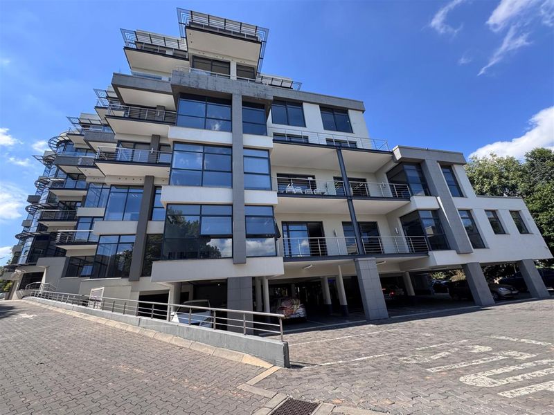 Modern multi-story office building featuring extensive glass facades, private balconies with stainless steel railings, and a paved ground-level covered parking area.