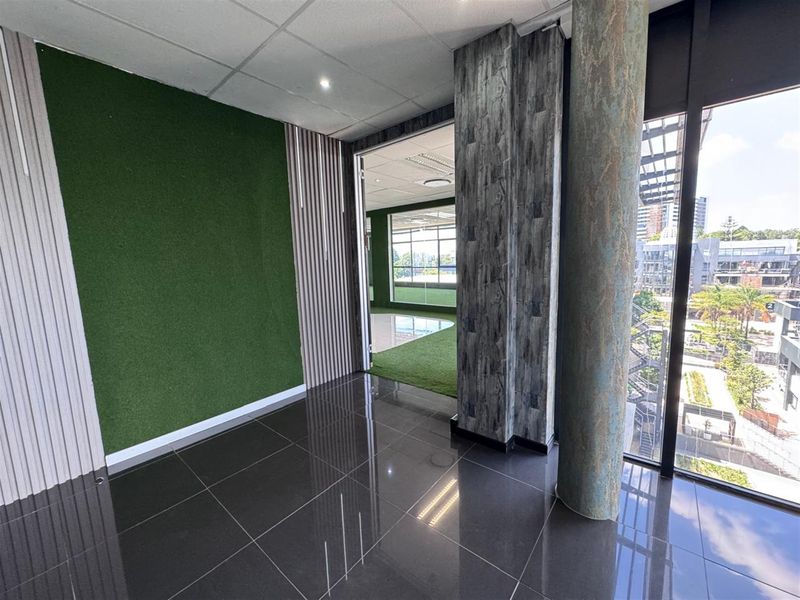 Modern office space featuring polished tile flooring, decorative wall paneling, a structural column, and large windows providing ample natural light and urban views.