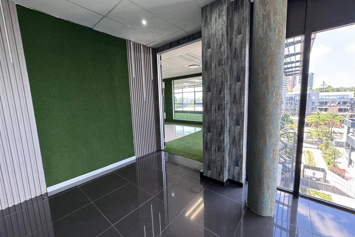 Modern office space featuring polished tile flooring, decorative wall paneling, a structural column, and large windows providing ample natural light and urban views.