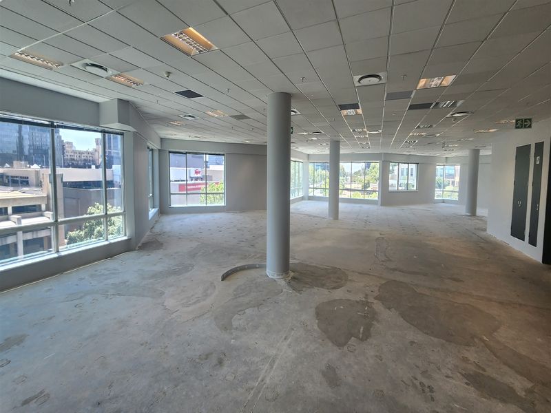 Spacious open-plan office area featuring large windows, structural columns, and a suspended ceiling, currently awaiting final flooring installation.