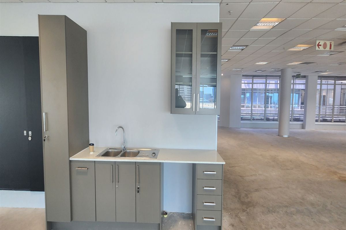A compact office kitchenette featuring modern grey cabinetry, a stainless steel sink, and a clean countertop, set within an open-plan office space.