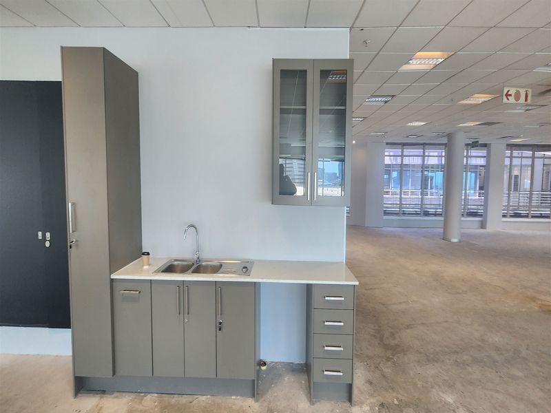 A compact office kitchenette featuring modern grey cabinetry, a stainless steel sink, and a clean countertop, set within an open-plan office space.