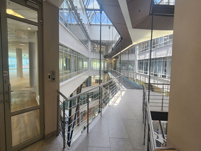 Modern office building interior featuring a multi-level atrium with a glass roof, suspended walkways, and extensive glass partitioning for a bright, open workspace.