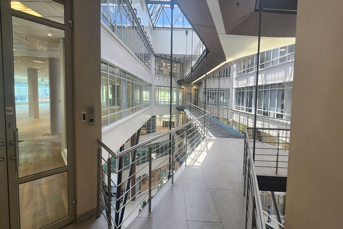 Modern office building interior featuring a multi-level atrium with a glass roof, suspended walkways, and extensive glass partitioning for a bright, open workspace.