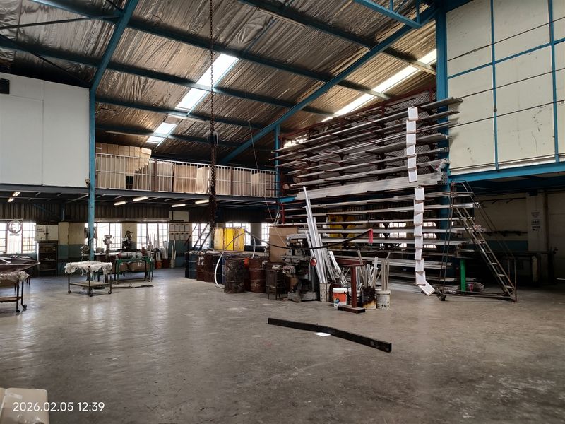 Spacious industrial warehouse featuring high ceilings with exposed steel trusses, a mezzanine level, concrete flooring, and integrated metal racking systems for storage.