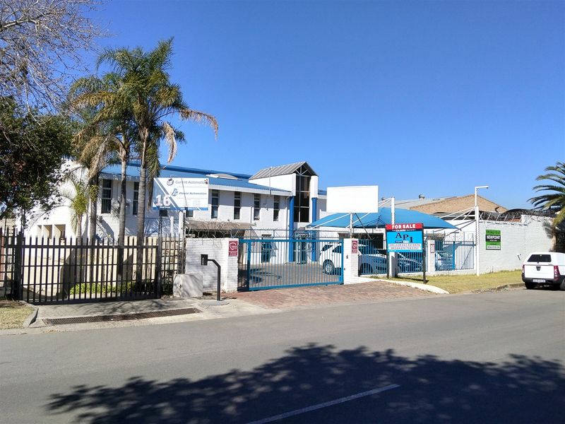 Front elevation of an industrial property featuring a secure gated entrance, paved driveway, and covered parking area.