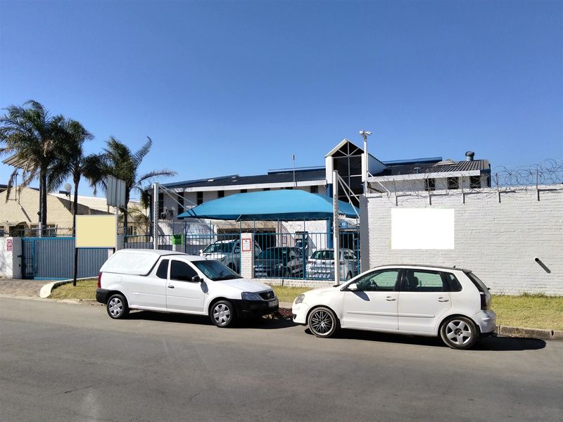 Front exterior view of the industrial property featuring a secure boundary wall with razor wire, metal gates, and a covered parking area.