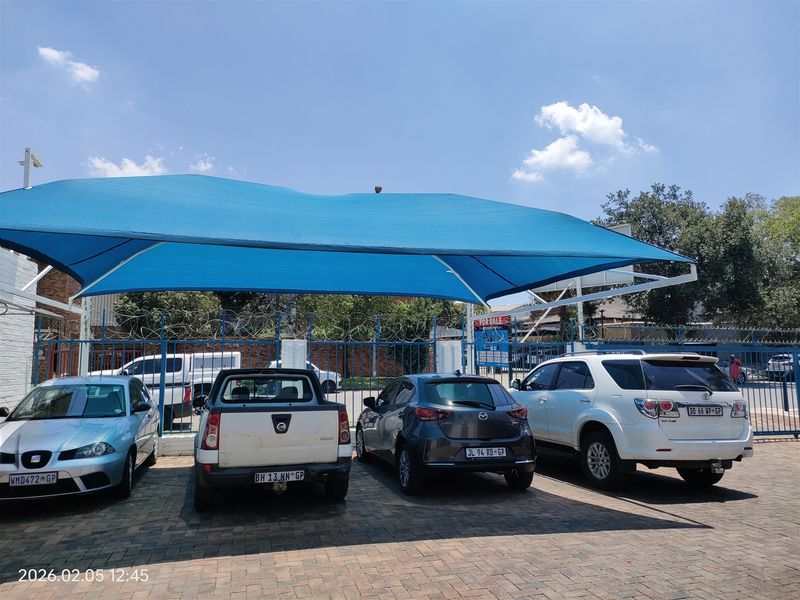 Industrial property exterior featuring a paved parking area covered by a large blue shade cloth structure and secured with perimeter fencing.