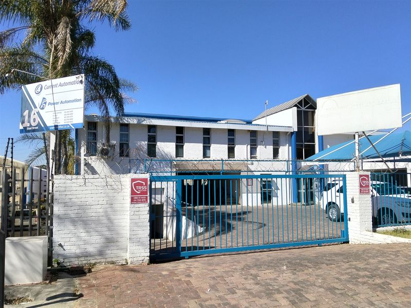 Front elevation of an industrial property featuring a secure gated entrance, paved driveway, and prominent business signage.