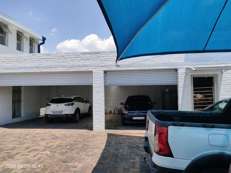 A functional double garage featuring white painted brickwork, roller shutter doors, and a paved driveway area shaded by a blue sail.