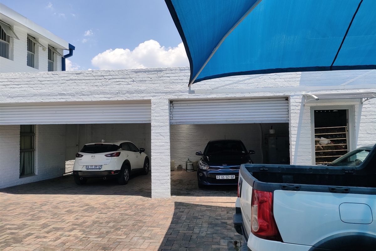 A functional double garage featuring white painted brickwork, roller shutter doors, and a paved driveway area shaded by a blue sail.