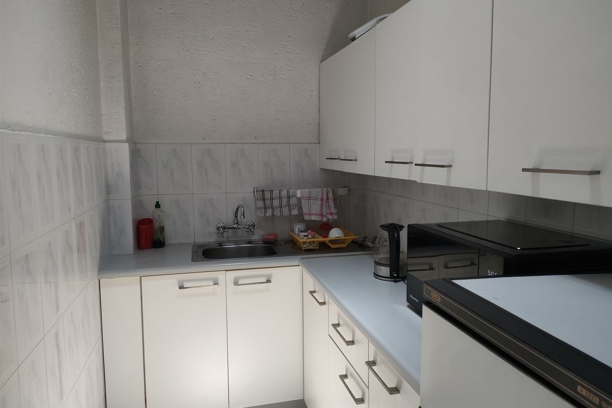 Compact kitchen area featuring white built-in cabinetry, laminate countertops, and a stainless steel sink with tiled backsplash.