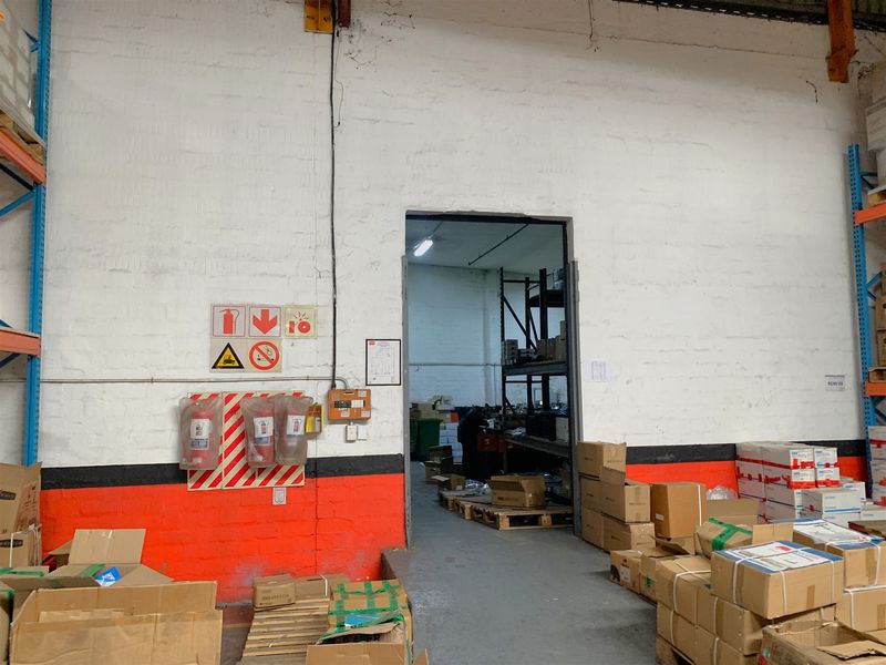 Industrial warehouse storage area featuring exposed brick walls, integrated shelving units, and essential fire safety equipment with direct access to an adjacent storage bay.
