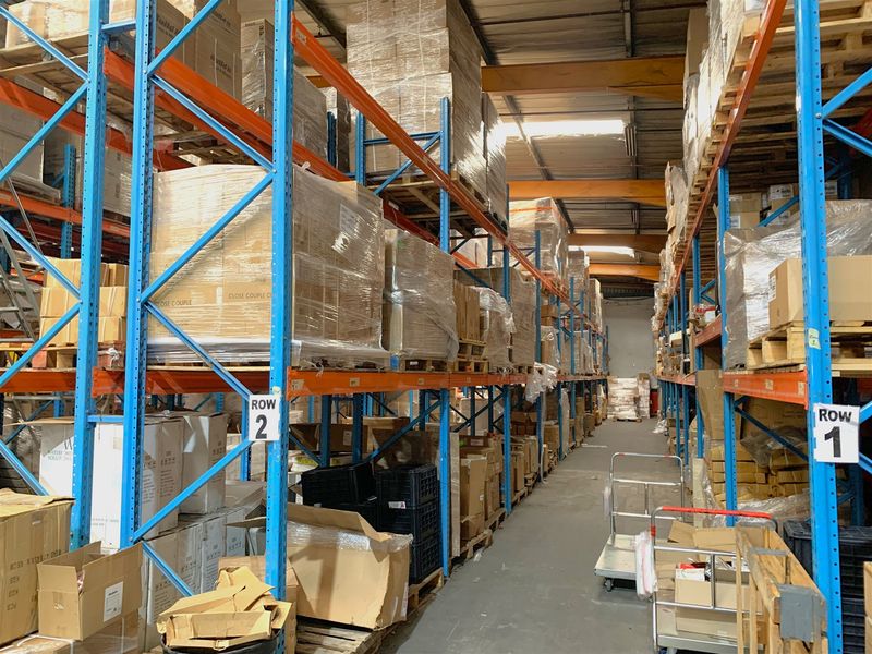 Industrial warehouse space featuring extensive steel racking systems, exposed roof trusses, and durable concrete flooring, optimized for high-density storage and logistics operations.