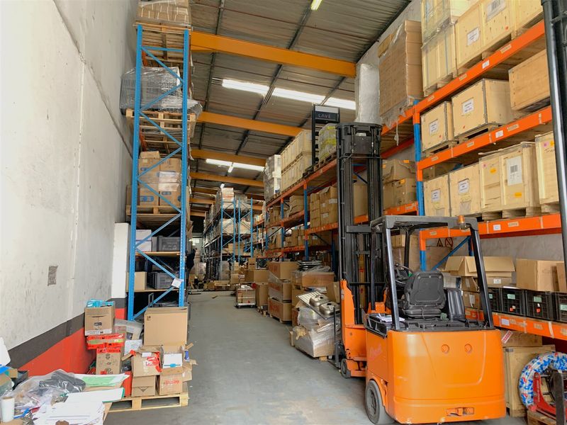Industrial warehouse space featuring high-clearance steel racking, exposed roof trusses, concrete flooring, and natural light provided by overhead skylights.