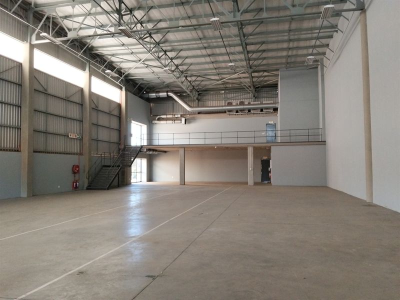 Spacious industrial warehouse unit featuring high ceilings with exposed steel trusses, a mezzanine level, concrete flooring, and integrated ventilation ducting.