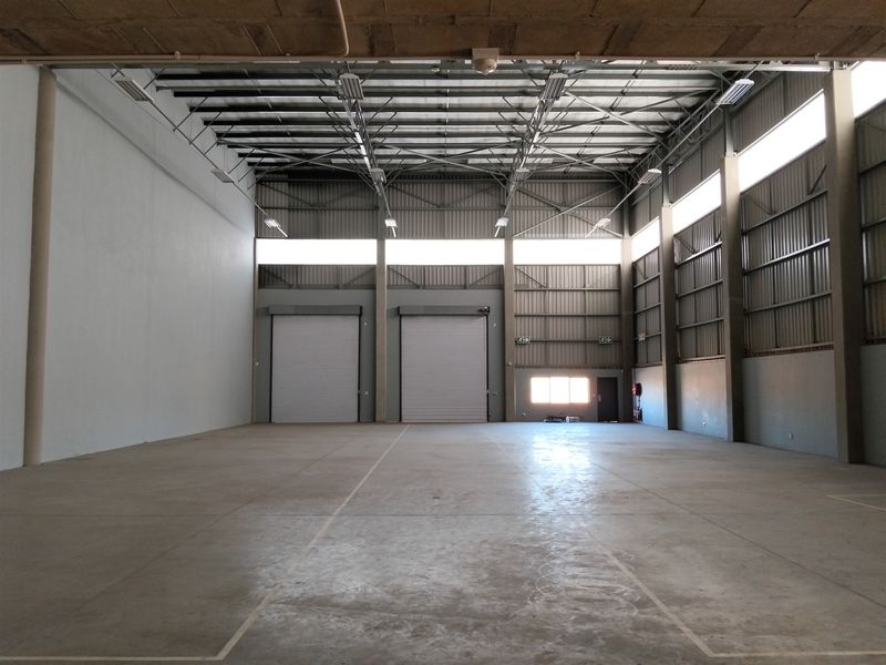 Spacious industrial warehouse unit featuring high ceilings, concrete flooring, and dual roller shutter doors, suitable for storage, logistics, or manufacturing operations.