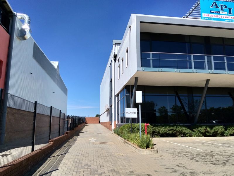 Industrial property exterior featuring a paved delivery access driveway, modern glass facade, and upper-level balcony with glass balustrade.