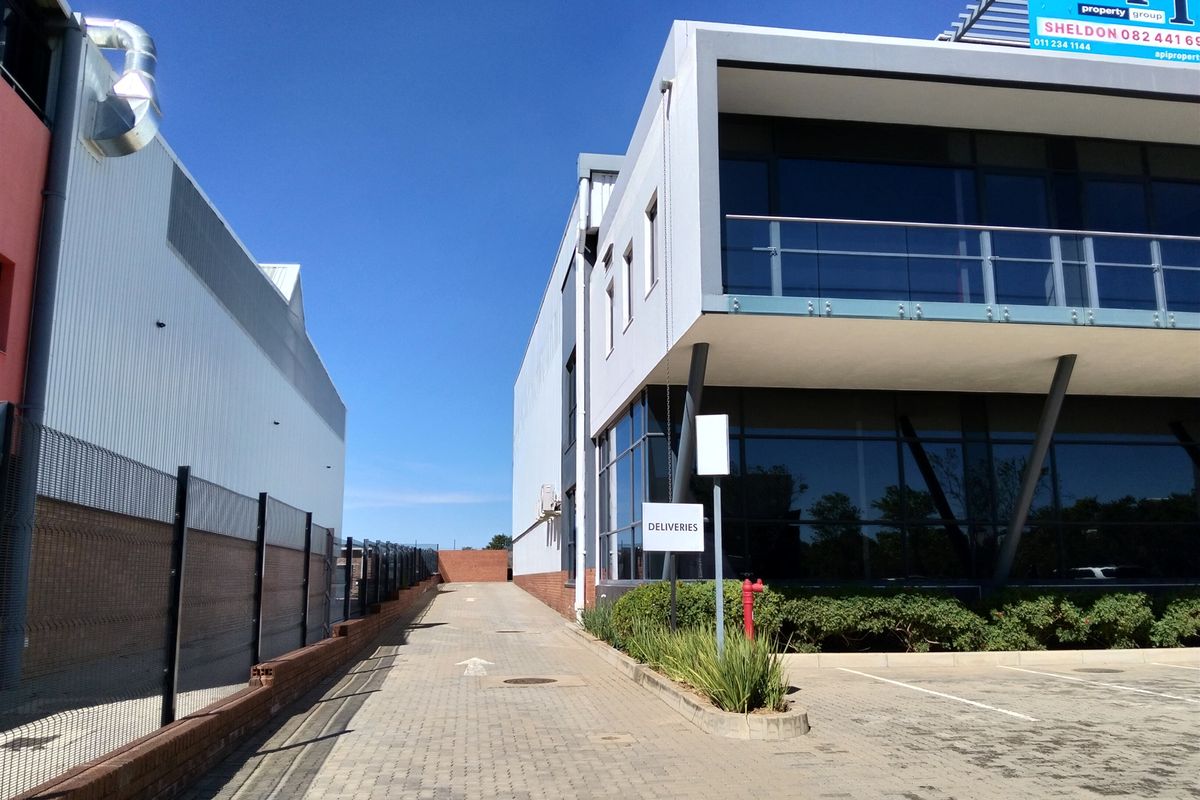 Industrial property exterior featuring a paved delivery access driveway, modern glass facade, and upper-level balcony with glass balustrade.