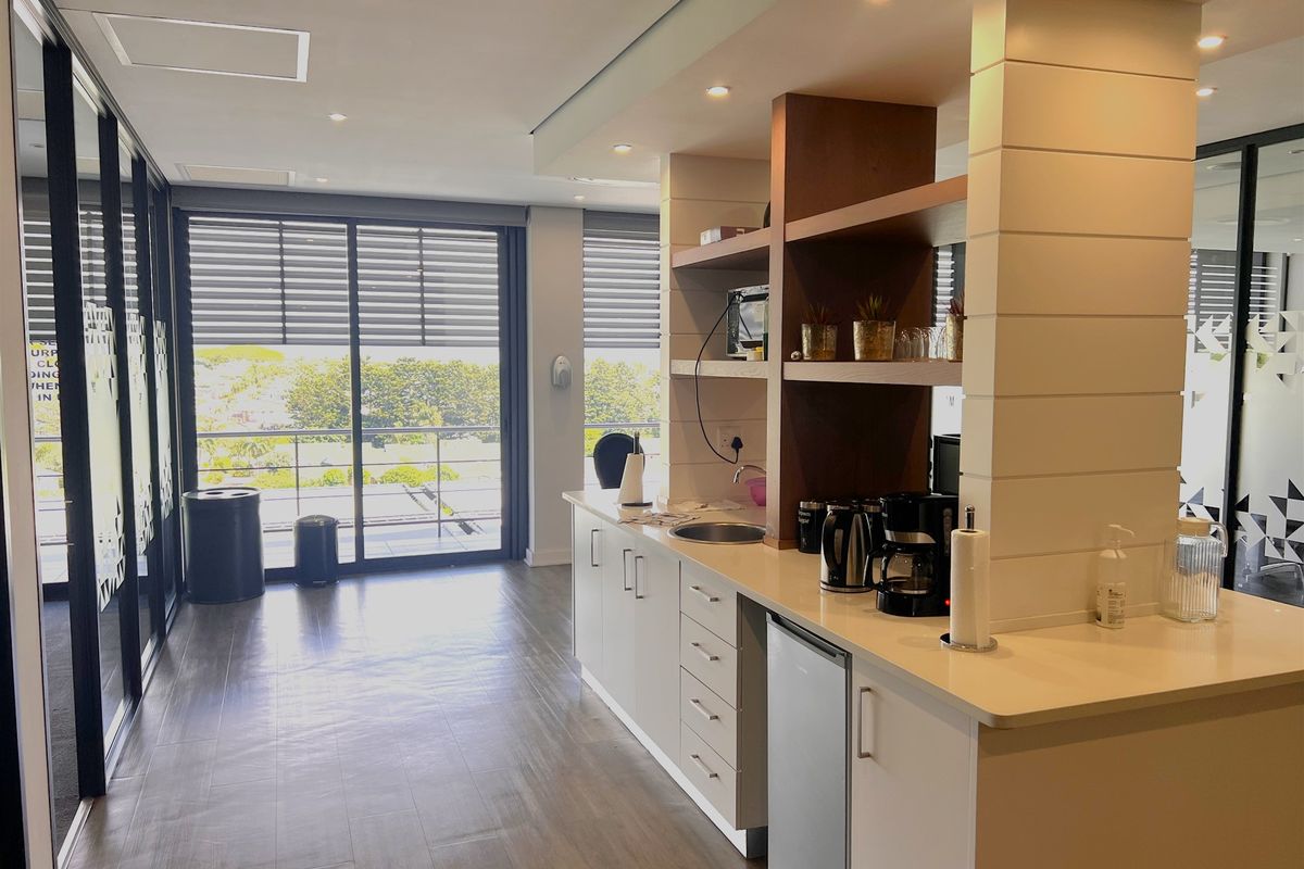 Modern office kitchenette featuring sleek white cabinetry, integrated sink, open shelving, and large sliding glass doors providing natural light and outdoor access.