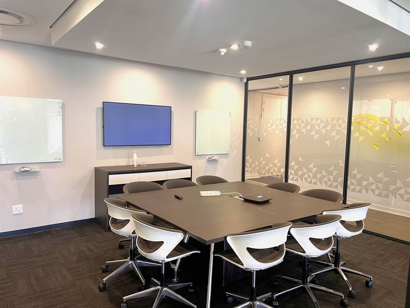 A modern, well-maintained office meeting room featuring a large central table, glass partition walls, and wall-mounted whiteboards.