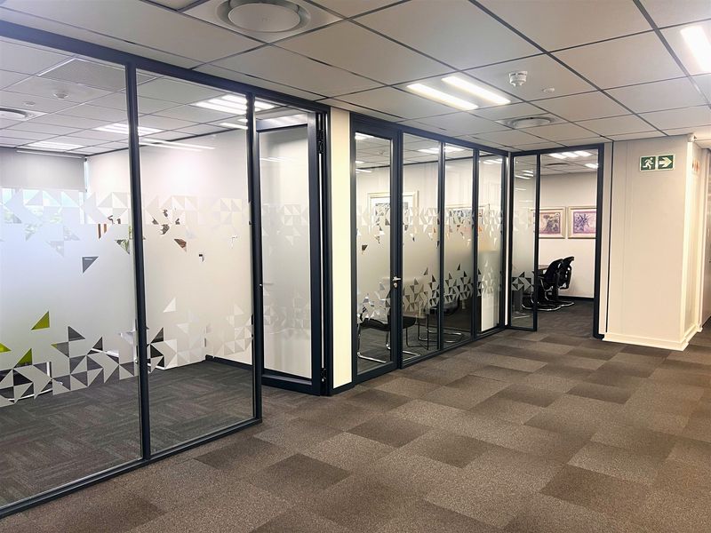 Modern office space featuring glass partition walls, suspended ceilings with recessed lighting, and professional carpet tiles throughout the workspace.