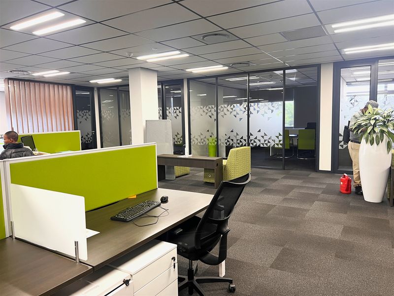 Modern open-plan office space featuring glass partitioned meeting rooms, suspended ceilings with recessed lighting, and professional carpet tile flooring.