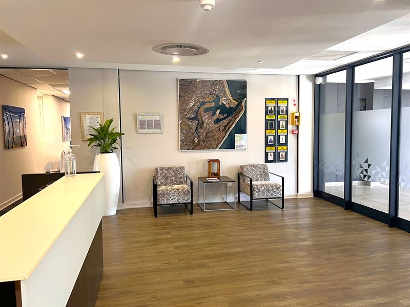A professional office reception area featuring a reception desk, laminate flooring, and a modern glass partition wall.