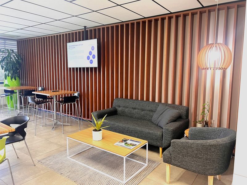 Modern office breakout area featuring a decorative slatted timber wall, tiled flooring, and a wall-mounted display screen.