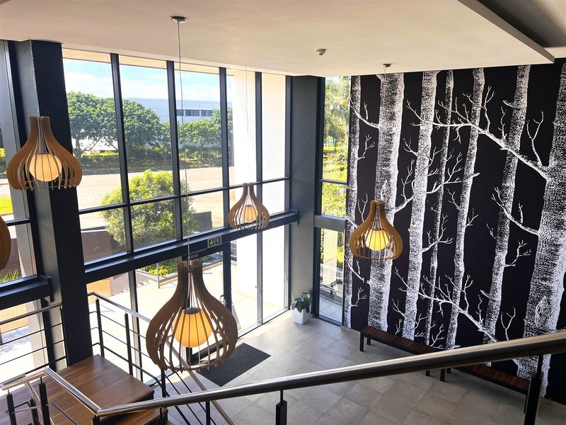 Modern office entrance lobby featuring double-volume ceilings, floor-to-ceiling glass windows, tiled flooring, and a contemporary staircase with metal railings.