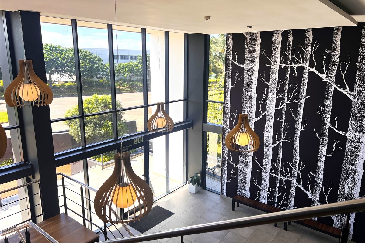 Modern office entrance lobby featuring double-volume ceilings, floor-to-ceiling glass windows, tiled flooring, and a contemporary staircase with metal railings.