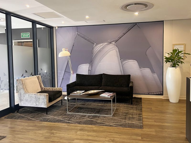 A modern office reception or waiting area featuring laminate flooring, a glass partition wall, and recessed ceiling lighting.