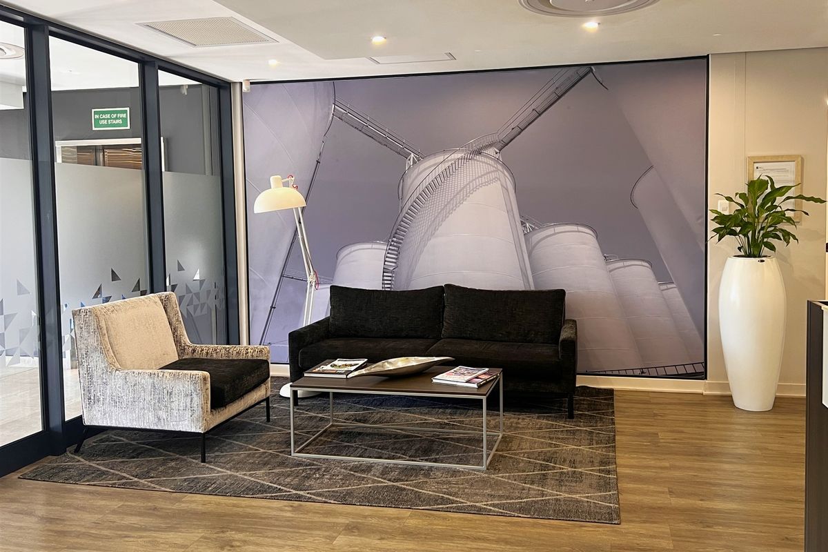 A modern office reception or waiting area featuring laminate flooring, a glass partition wall, and recessed ceiling lighting.