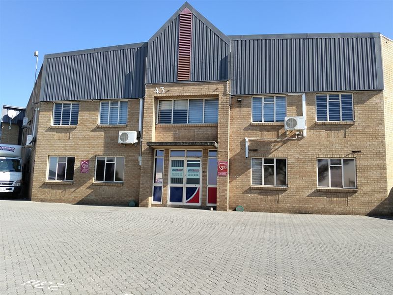 Front elevation of a two-story industrial brick building featuring a paved forecourt, metal roofing, and multiple split-system air conditioning units.