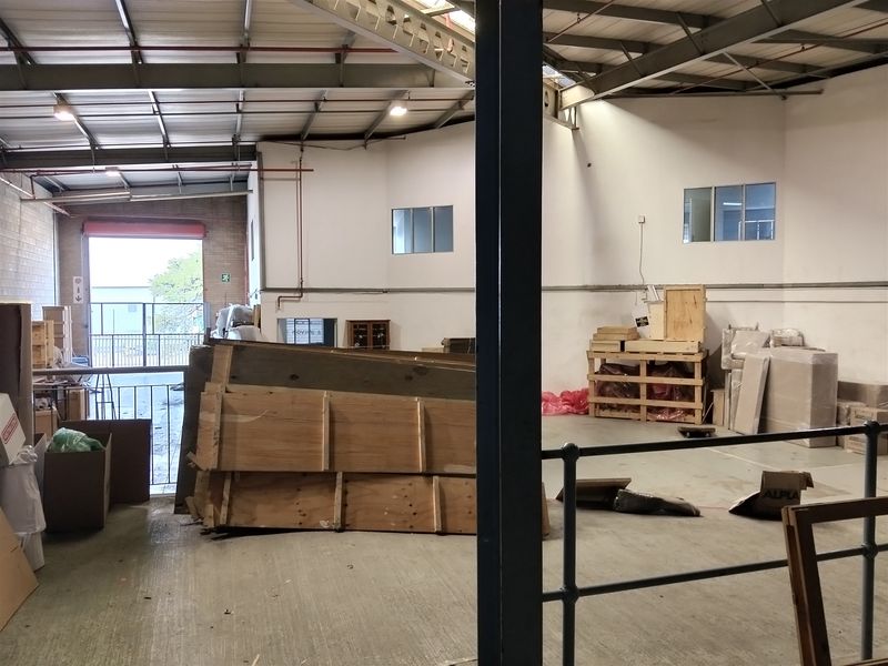 Spacious industrial warehouse area featuring exposed steel roof trusses, concrete flooring, and a large roller shutter door, suitable for storage or light manufacturing.
