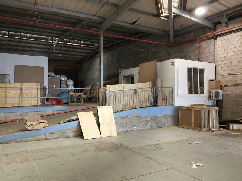 Industrial warehouse space featuring exposed steel trusses, fire sprinkler system, concrete flooring, and a raised loading ramp with metal safety railing.
