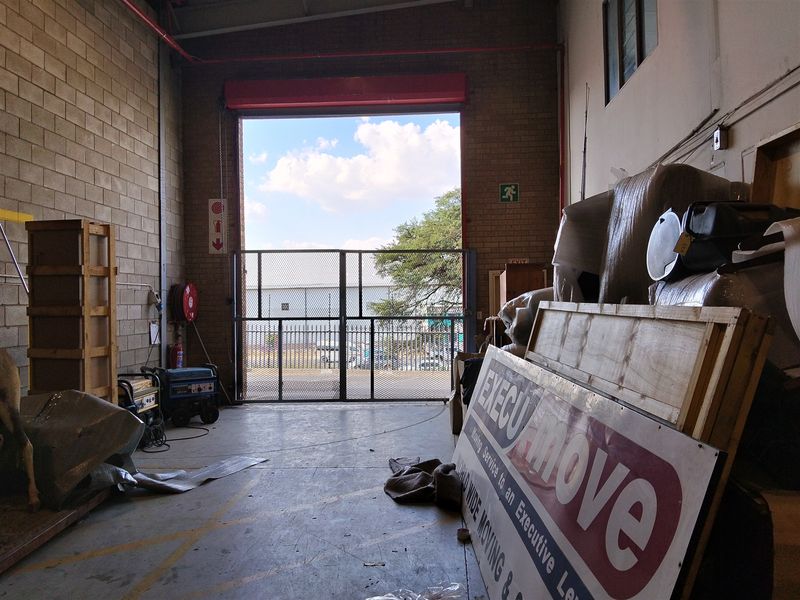 Industrial utility space featuring high ceilings, exposed brick walls, a large roller shutter door, and integrated fire safety equipment.
