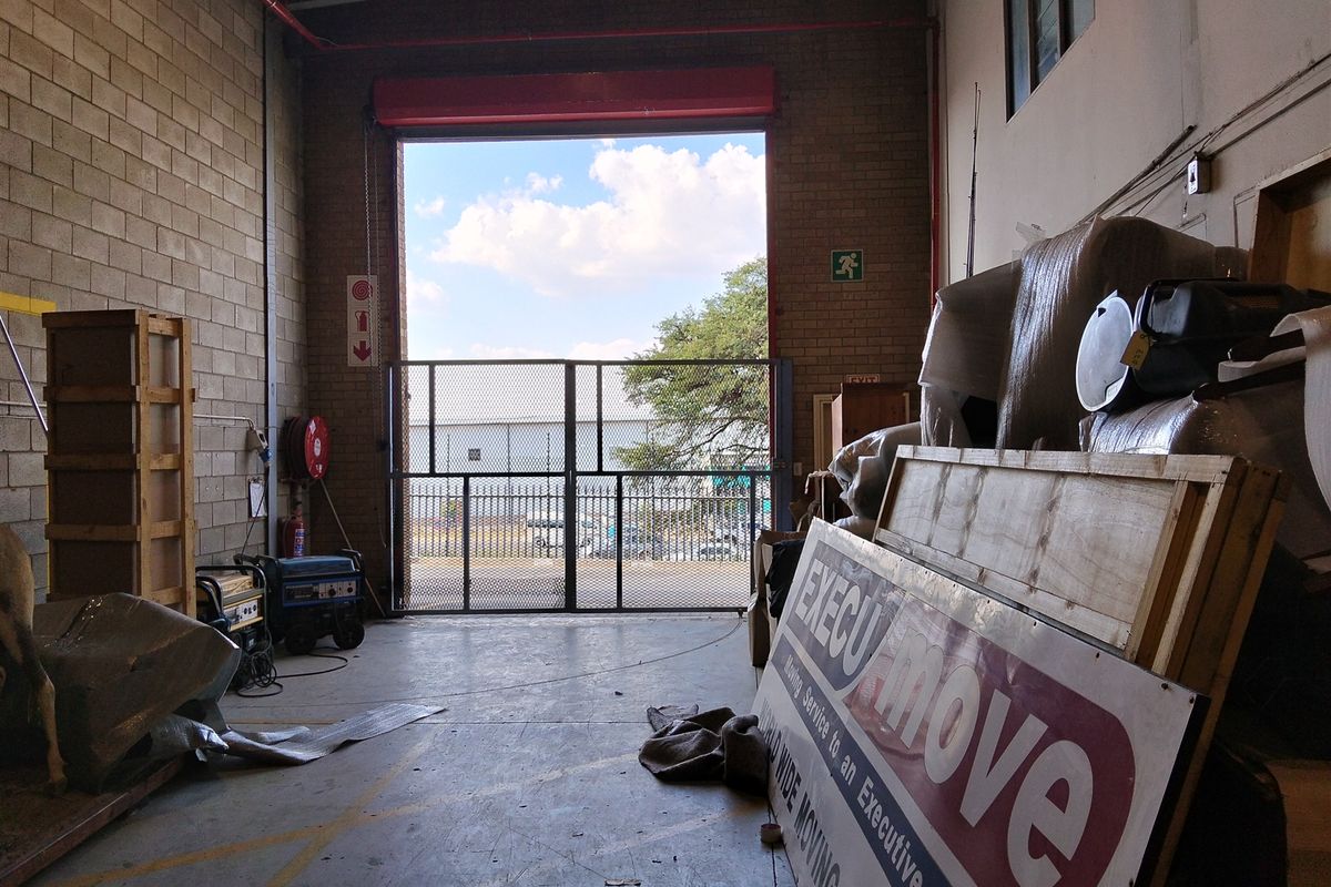 Industrial utility space featuring high ceilings, exposed brick walls, a large roller shutter door, and integrated fire safety equipment.