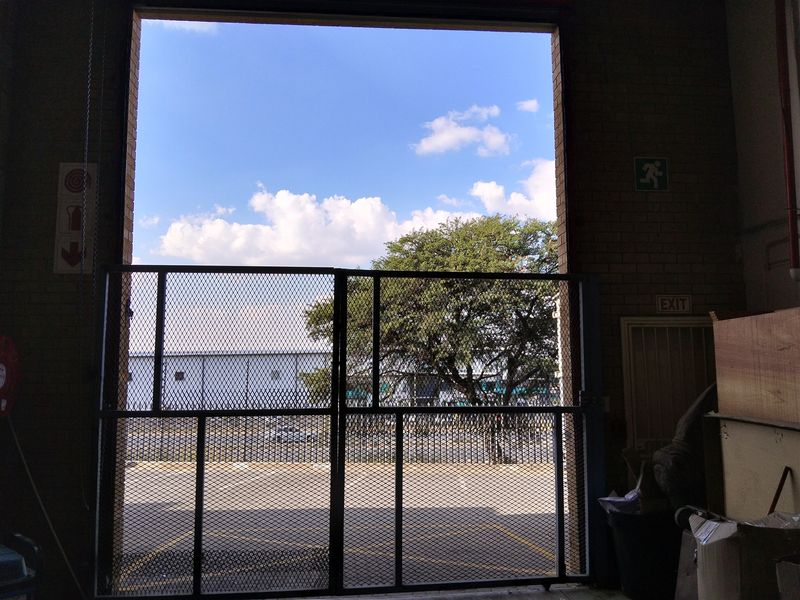 Industrial garage space featuring a large metal security gate, exposed brick walls, and clear emergency exit signage.