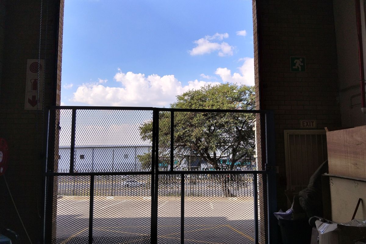 Industrial garage space featuring a large metal security gate, exposed brick walls, and clear emergency exit signage.