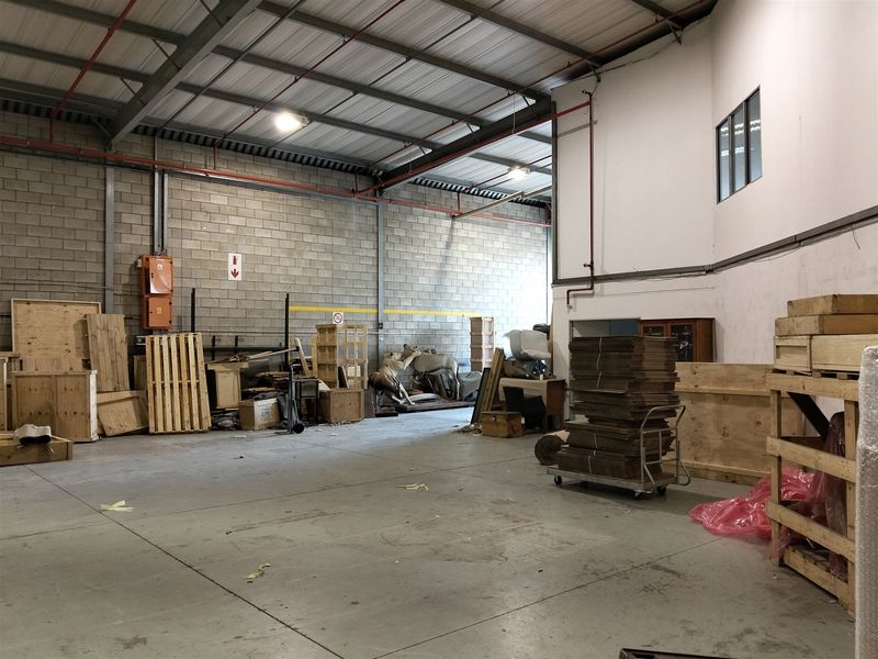 Spacious industrial utility area featuring exposed steel roof trusses, concrete block walls, and durable concrete flooring, suitable for storage or workshop use.