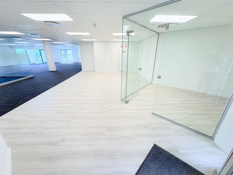 Modern open-plan office space featuring glass partitioning, suspended ceilings with recessed lighting, and a combination of laminate and carpet flooring.
