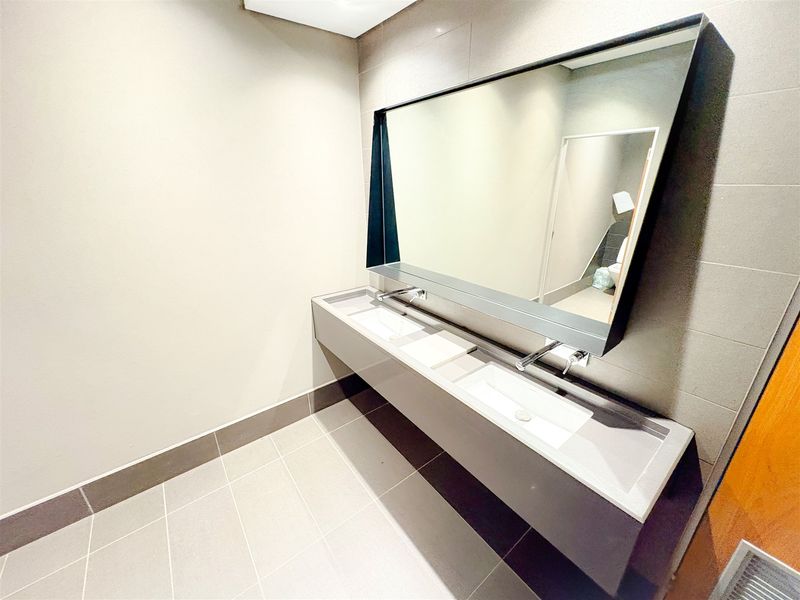 Modern office bathroom featuring a sleek double vanity with wall-mounted faucets and a large integrated mirror.