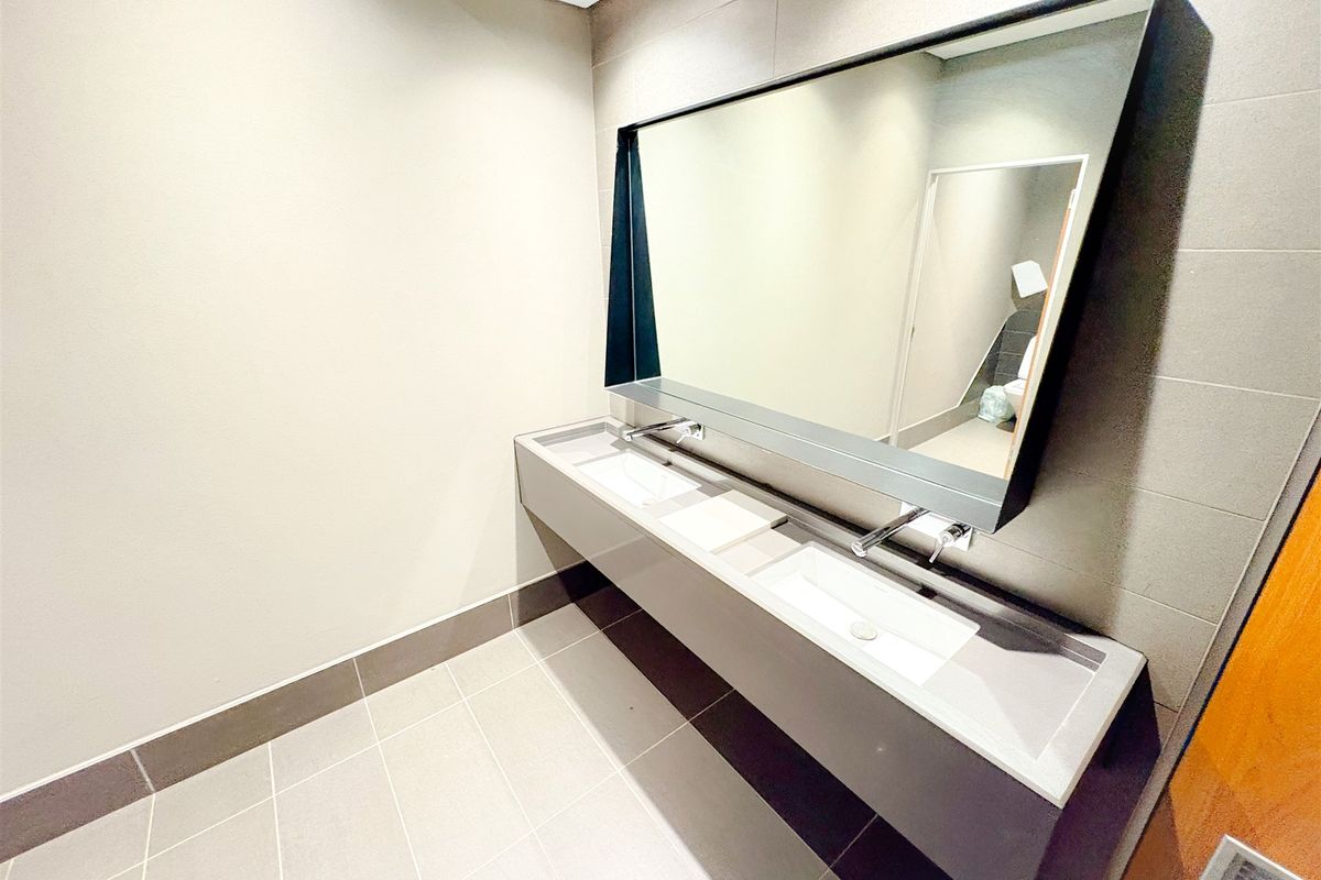 Modern office bathroom featuring a sleek double vanity with wall-mounted faucets and a large integrated mirror.
