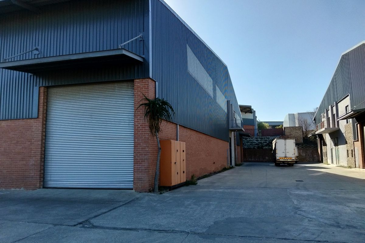 Rear industrial yard featuring a large roller shutter door, brick and metal cladding construction, and concrete hardstand area for vehicle access.
