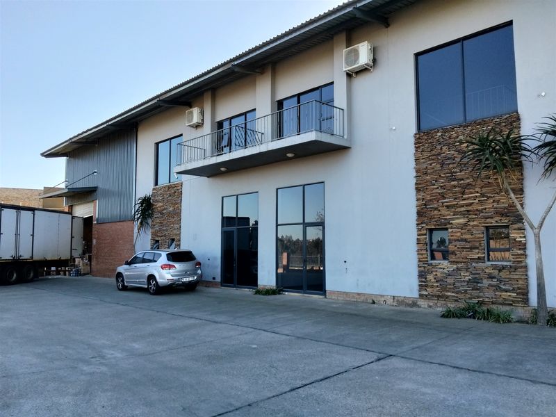 Industrial property exterior featuring a concrete driveway, stone cladding accents, a balcony, and modern aluminium-framed windows and doors.