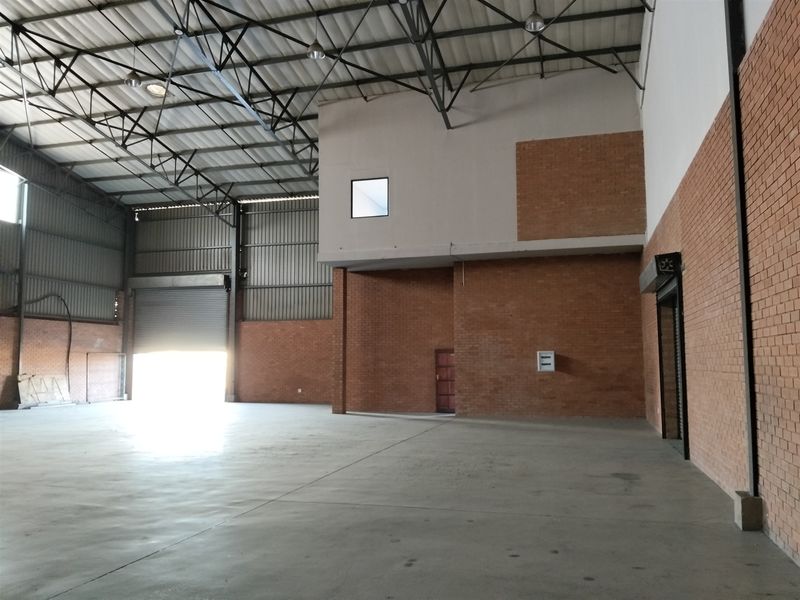 Spacious industrial warehouse unit featuring high ceilings with exposed steel trusses, concrete flooring, and a large roller shutter door for easy access.