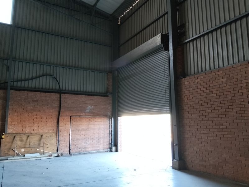 Spacious industrial utility area featuring high ceilings, exposed steel structure, face brick walls, concrete flooring, and a large roller shutter door for vehicle access.