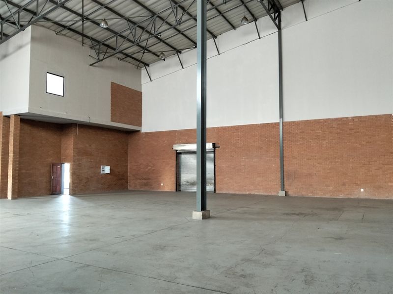 Spacious industrial warehouse unit featuring high ceilings with exposed steel trusses, concrete flooring, and a large roller shutter door for easy access.