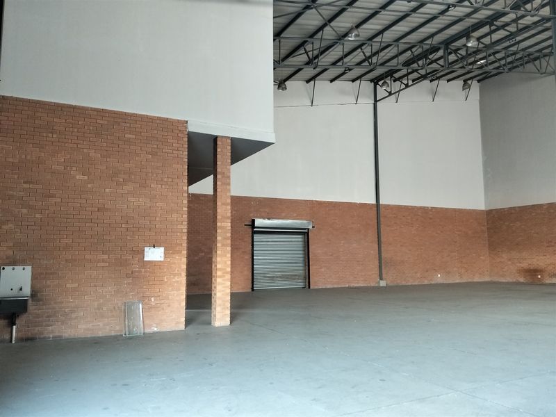 Spacious industrial warehouse unit featuring high ceilings with exposed steel trusses, concrete flooring, and a secure roller shutter door access.